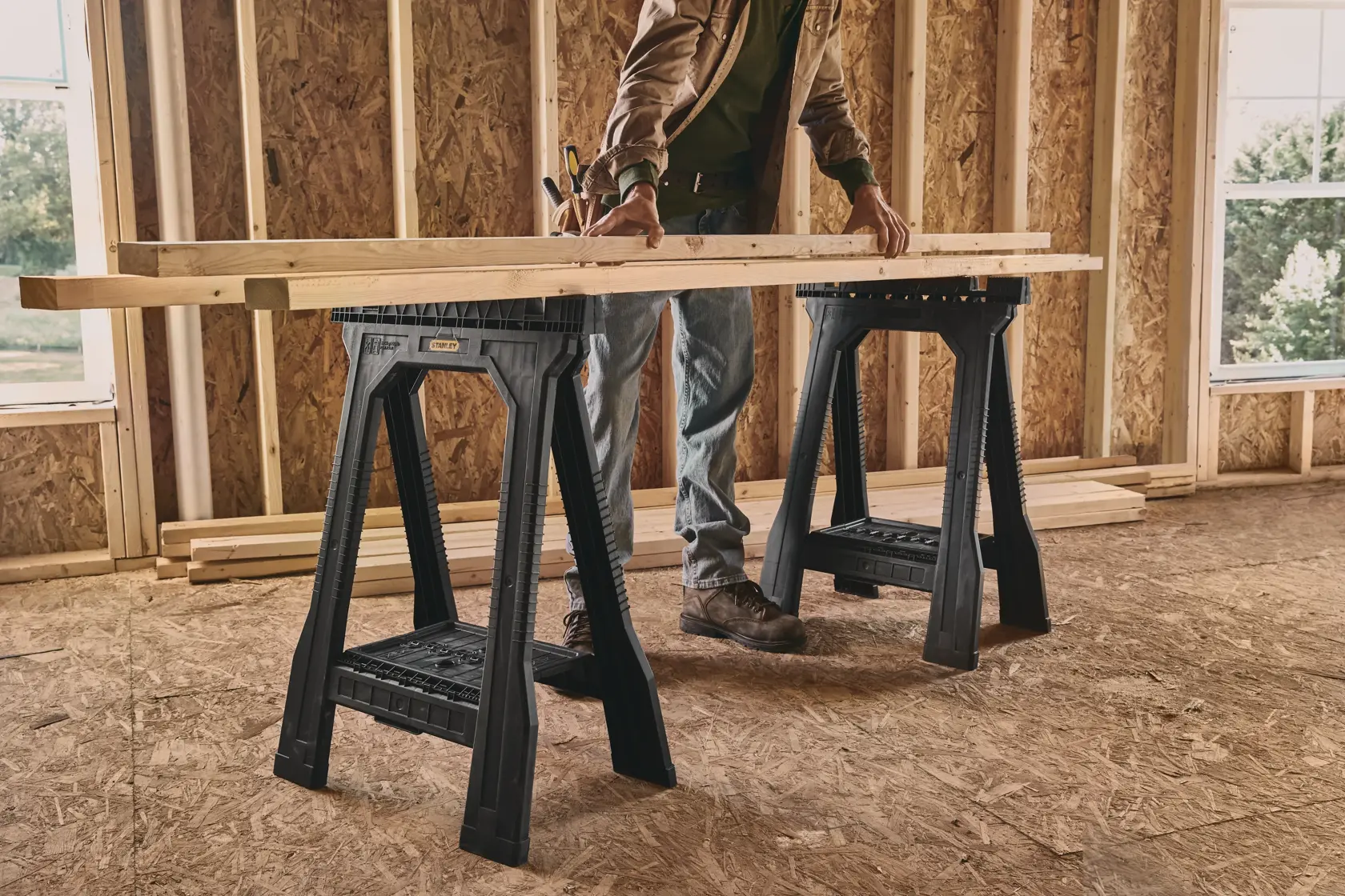 STANLEY STST60952 black folding sawhorses supporting wooden boards in a construction room, photographed from the side.
