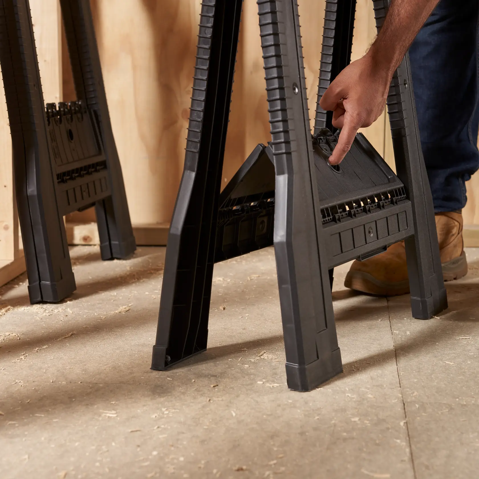 STANLEY STST60952 black plastic sawhorse in workshop, person unfolding leg, side angle.