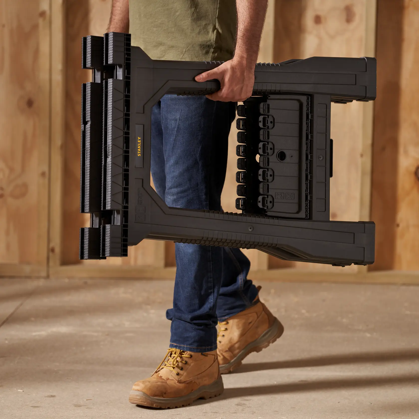 Stanley STST60952 black folding sawhorse carried by person in work boots and jeans.