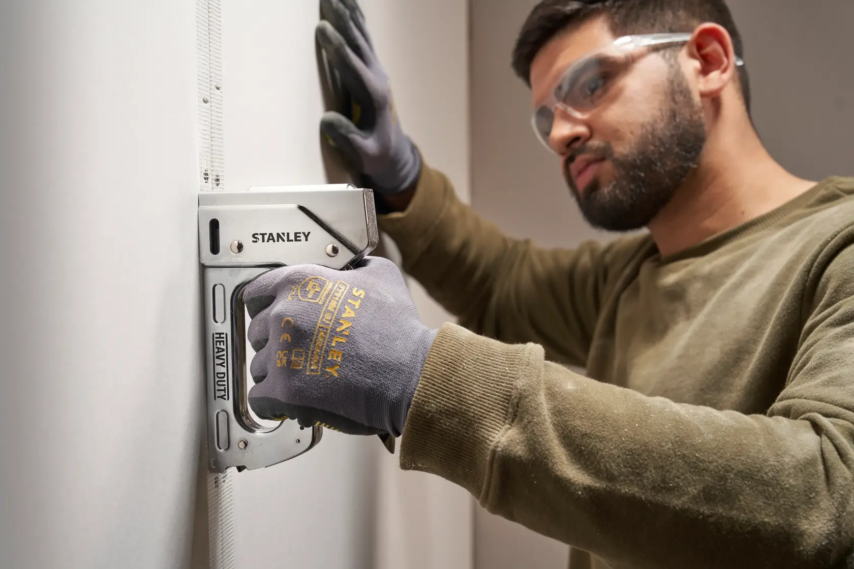 Stanley TR110 heavy duty staple gun held by gloved hand against wall, close-up photography.