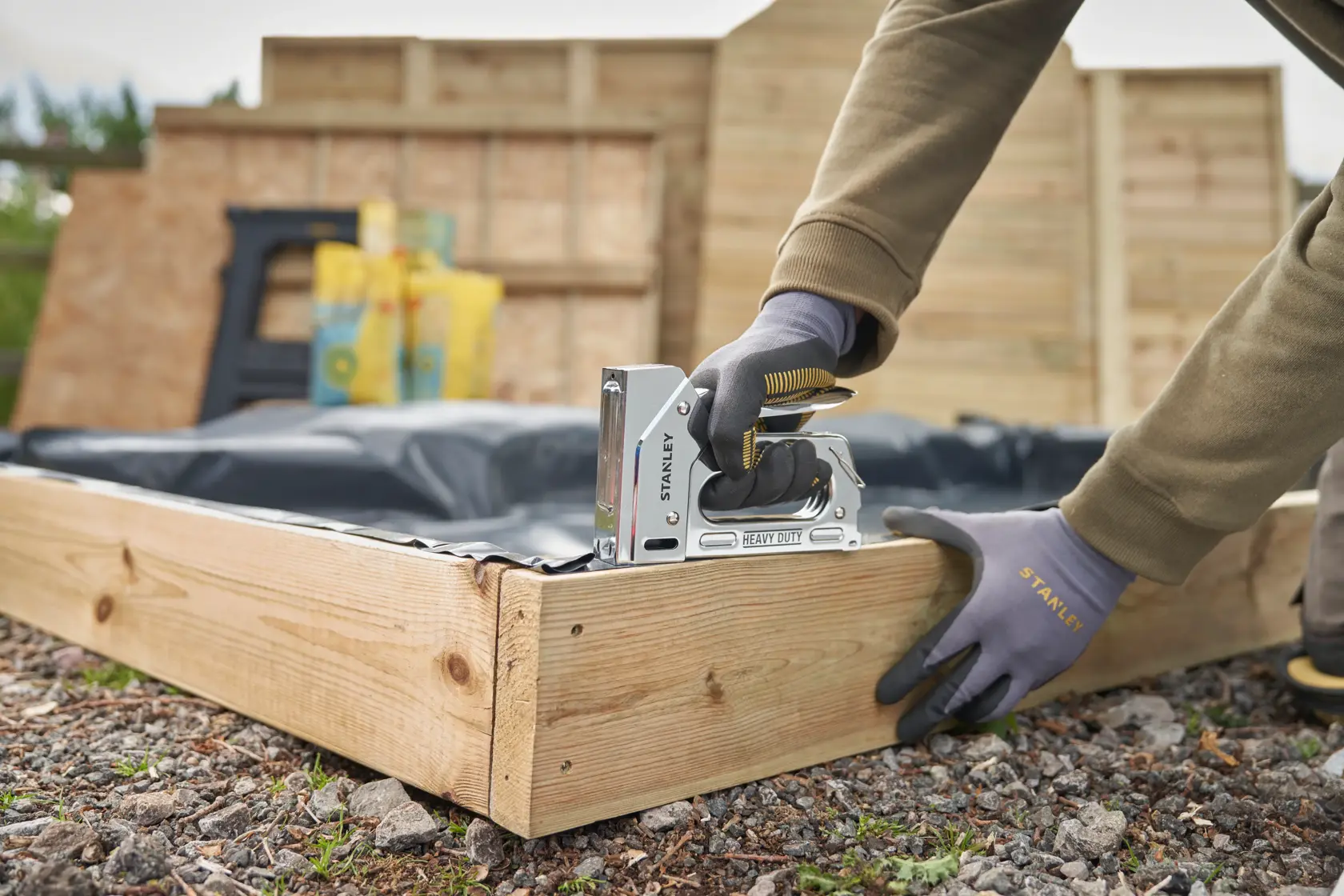 STANLEY TR110 heavy duty staple gun in use securing plastic to a wooden garden frame outdoors.