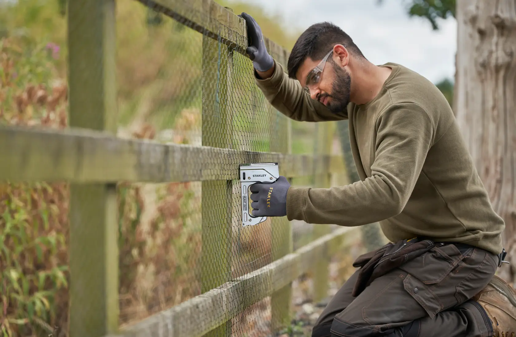 Stanley TR110 staple gun used to attach wire mesh to wooden fence outdoors.