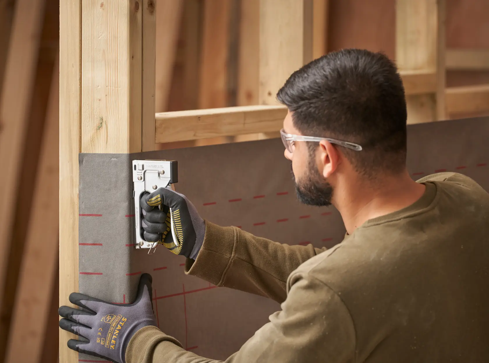 Photo of STANLEY TR45 staple gun in use, person wearing gloves staples sheeting to wooden frame.